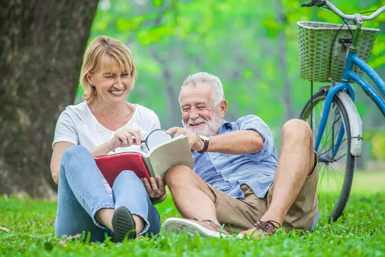 Happy elderly couple with smiling face enjoying together, reading a book with magnifying glass in the park, spending time and relaxing time concept. | North Houston